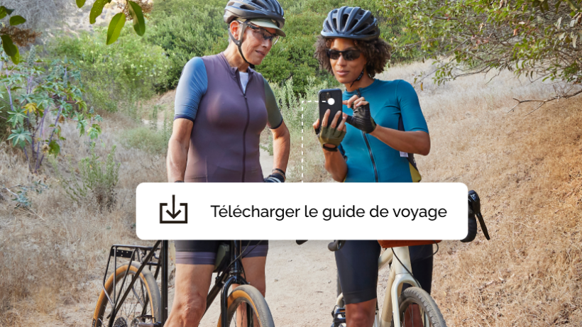 Deux femmes faisant une promenade à vélo, marquant une pause pour télécharger une application de guide de voyage offerte par une campagne Mailchimp.