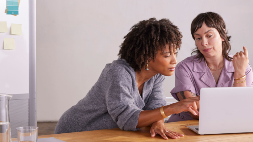 Two women in front of a laptop, planning out their small business’s social media calendar.